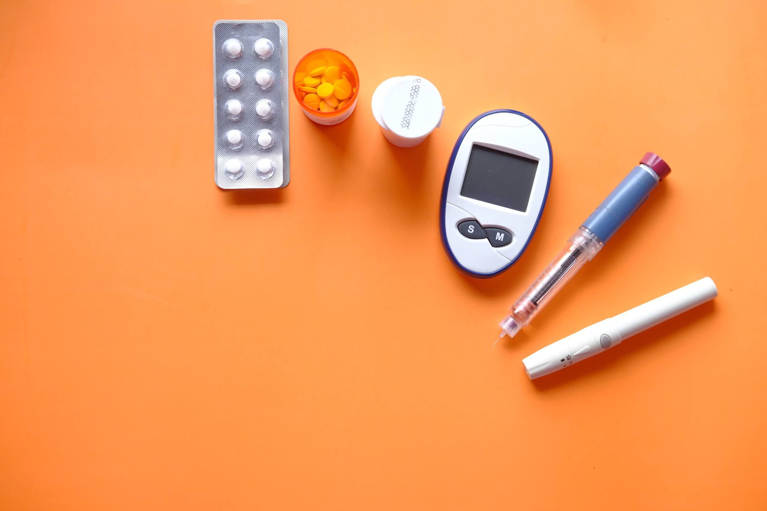 Insulin pen, diabetes measurement tools and pills on orange background