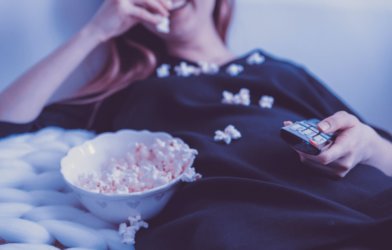 Woman eating popcorn holding remote control while watching TV
