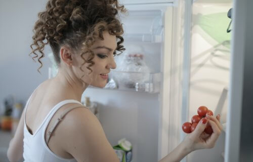 Woman looking through refrigerator holding tomatoes