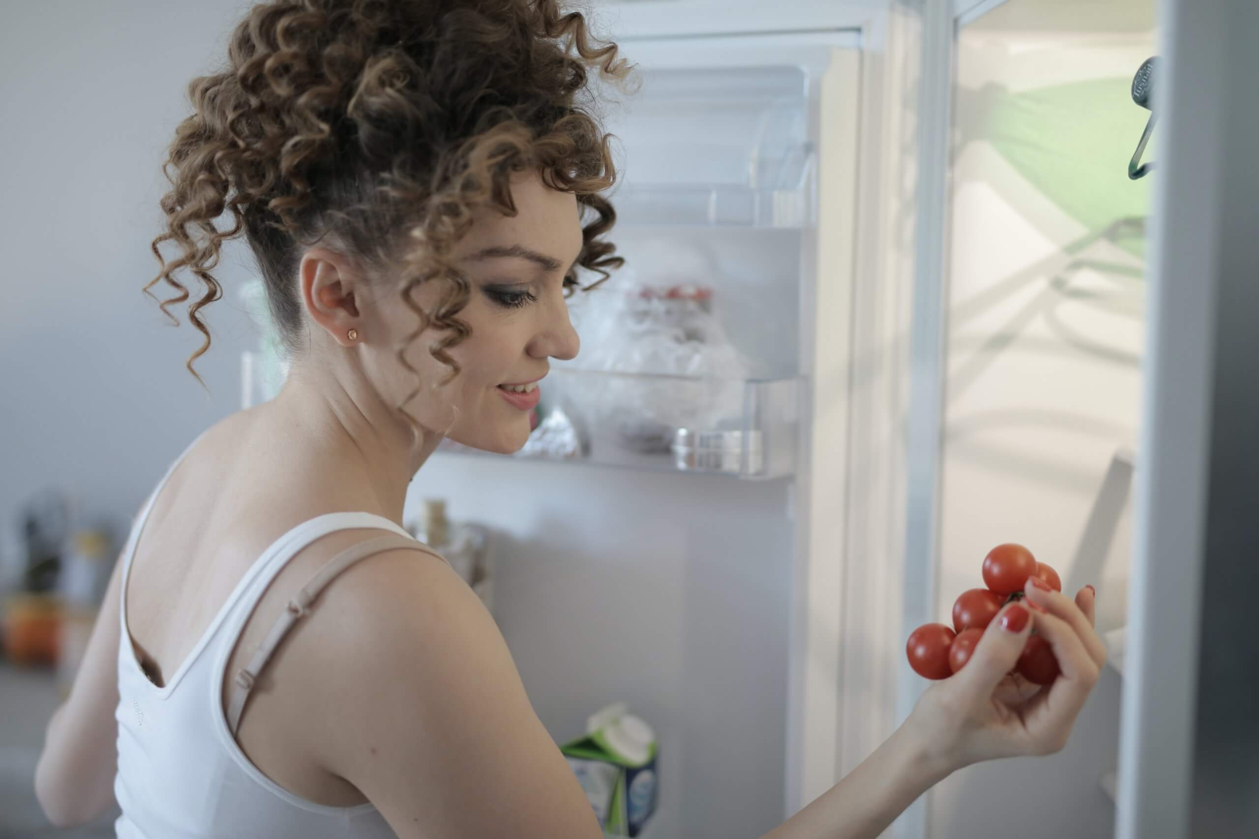 Woman looking through refrigerator holding tomatoes