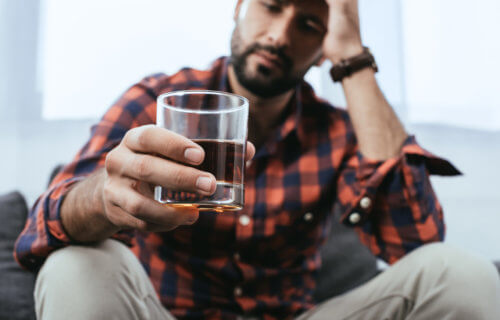 Man drinking glass of whiskey or alcohol, feeling stressed