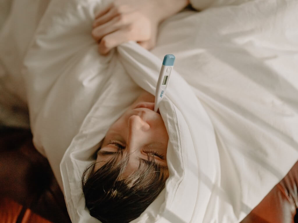 Man sick in bed with thermometer in mouth