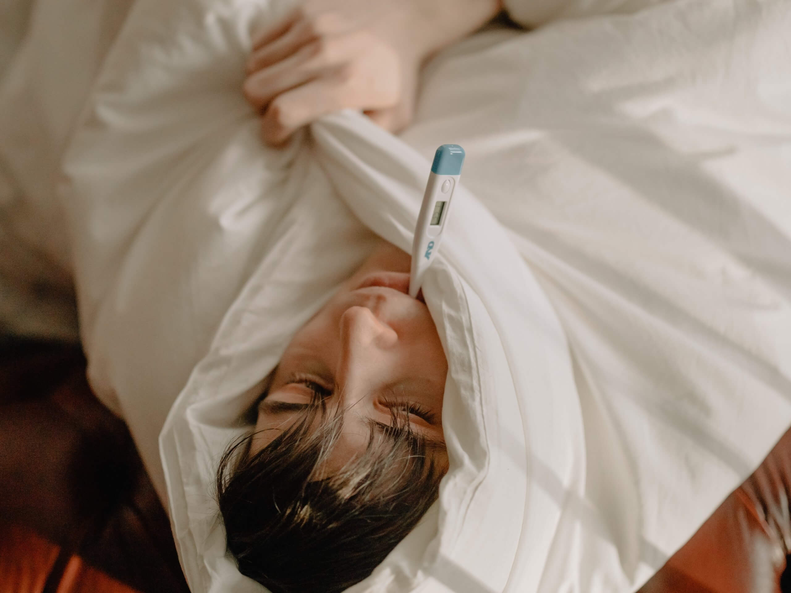 Man sick in bed with thermometer in mouth